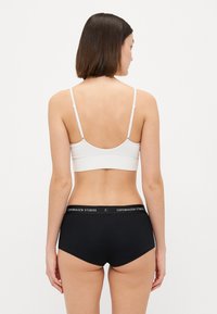 Hvit ribbet bralette med tynne stropper og svarte høyhalsede shorts med en merket midjebånd. Enkelt design, myk tekstur.