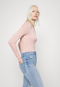 Top de manga longa, ajustado, de cor rosa claro com uma textura suave, combinado com jeans de cintura alta em azul claro, com bolsos laterais.