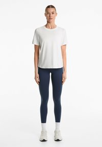 Maglietta bianca a maniche corte con scollo rotondo abbinata a leggings blu navy. Il modello indossa sneakers bianche con calzini bianchi.