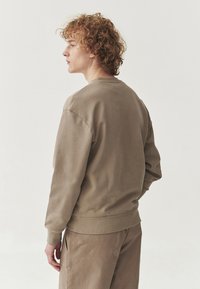 Felpa in cotone marrone con scollatura a girocollo, polsini a costine e pantaloni coordinati. Tessuto morbido, vestibilità rilassata, design minimalista.