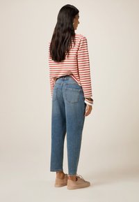Camisa de manga larga a rayas con líneas horizontales rojas y blancas, combinada con jeans de tiro alto en azul claro y zapatillas beige. Ajuste casual.