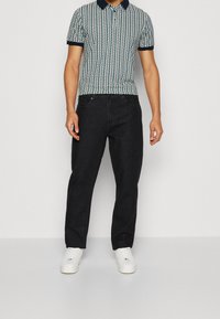Polo avec col marine et motif en vert et blanc, associé à un jean noir droit et des baskets blanches.