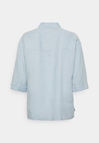 Ljust blå linnekjorta med krage, korta ärmar och en avslappnad passform. Har en horisontell söm över ryggen.