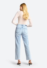 Jeans de corte recto en azul claro con una cintura alta, que cuentan con dos bolsillos traseros y dobladillos sin terminar, combinados con una camiseta ajustada de manga larga.