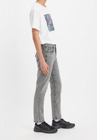 Camiseta blanca con un estampado gráfico colorido, combinada con jeans de mezclilla grises. Zapatillas deportivas negras con una superficie texturizada.