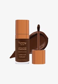 Brun væske concealer i en klar flaske med kobberlokk, med en doe-foot applikator. Inkluderer en prøve av matchende produkt.