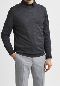 Mörkgrå stickad tröja med rund halsringning, kombinerad med ljusgrå skräddarsydda byxor. Tröjan har en subtil textur och ribbade ärmslut.