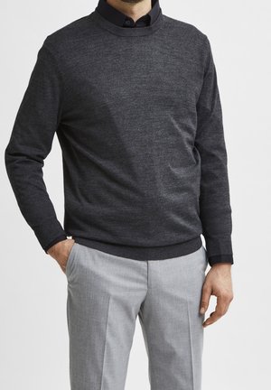 Dunkelgrauer Strickpullover mit Rundhalsausschnitt, kombiniert mit hellgrauen taillierten Hose. Der Pullover hat eine dezente Textur und Rippbündchen.