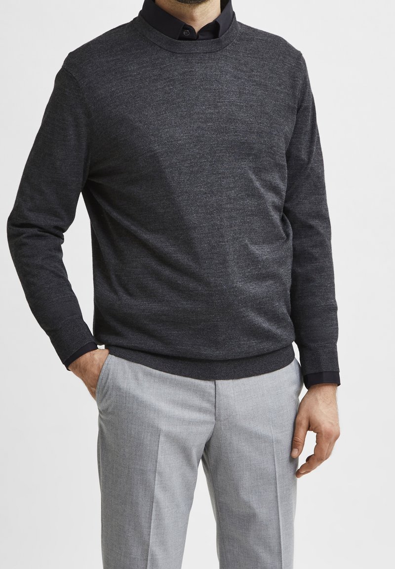 Mörkgrå stickad tröja med rund halsringning, kombinerad med ljusgrå skräddarsydda byxor. Tröjan har en subtil textur och ribbade ärmslut.