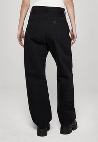 Pantalones de mezclilla negros con un ajuste relajado, cintura alta, dos bolsillos traseros y una sutil marca en la pretina. Tela texturizada.