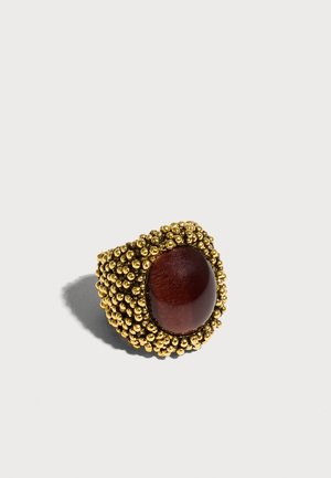 Gold beaded ring with a large smooth dark red oval stone in the center, casting a shadow on a light background.