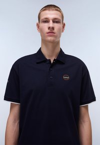 Marinblå piké skjorta i bomull med knäppning i tre knappar, korta ärmar och en cirkulär logodetalj på bröstet. Strukturerad kvalitet.