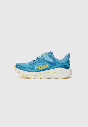 Blauer Sportschuh mit Mesh-Obermaterial, gelbem Logo, verstellbarem Riemen, dicker weißer Sohle und strukturiertem Gummiaußensohle für besseren Halt.