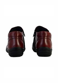 Røde lædersko med en glat overflade, udstyret med sorte gummisåler og sidelommer for nem påføring. Baghavede billedet viser runde hæle.