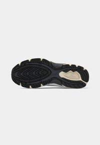 Black and beige rubber outsole of a running shoe with patterned treads and a visible Mizuno logo on the heel section.