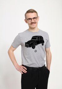 Šedé tričko s krátkým rukávem, které má černou konturovou grafiku klasického auta. Nositeli oblečení jsou černé kalhoty a pásek, stojící na neutrálním pozadí.