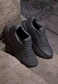 Pair of black athletic sneakers with laces placed on stone steps near a manhole cover on a stone pavement.