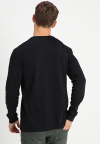Schwarzes Langarmshirt aus weichem Baumwollmaterial mit Rundhalsausschnitt und schlichter Gestaltung. Der Rücken hat keine ausgeprägten Muster oder Akzente.