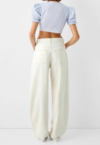 Světle modrý zkrácený top s nafouknutými rukávy a elastickými manžetami, spárovaný s vysokými krémovými kalhotami s širokými nohavicemi, které mají zadní kapsy a švy.