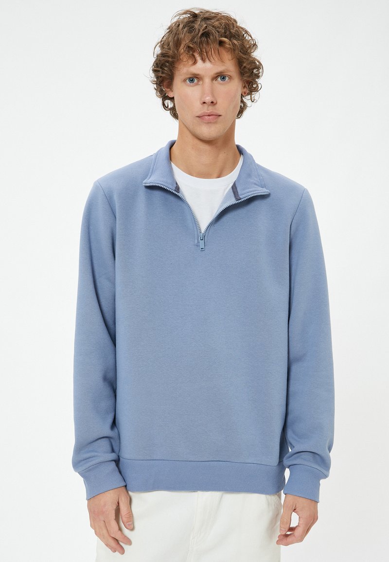 Felpa con zip di colore azzurro chiaro, realizzata in tessuto morbido, con colletto alto, polsini e orlo a costine, e una vestibilità comoda.