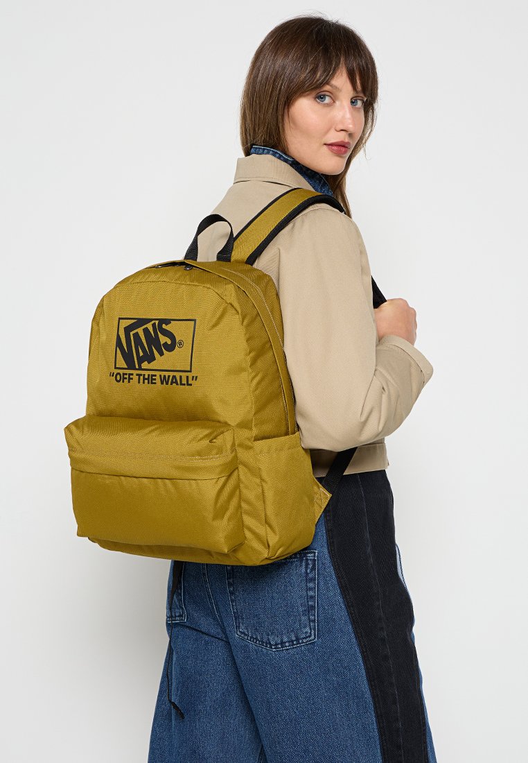 Mochila amarilla de Vans con logotipo negro, forma rectangular, textura de tela, correas acolchadas, bolsillo frontal y cierre de doble cremallera.