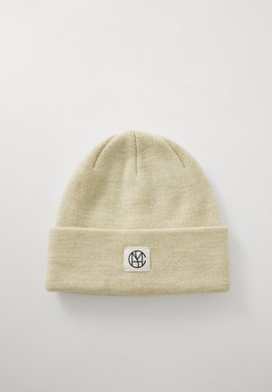 Light beige knit beanie with a folded cuff, featuring a square patch with a black logo in the center. Soft texture, simple design.