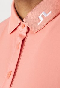 Rosa polo skjorta med ribbad krage och vit logotyp. Slät tyg med knappstängning fram för stängning.