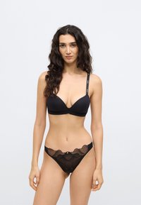 Σετ μαύρου εσωρούχου που περιλαμβάνει ένα απαλό, μη ενισχυμένο σουτιέν με ρυθμιζόμενες τιράντες και μπικίνι με δαντέλα, κυματιστά άκρα και διακοσμητικό στοιχείο.