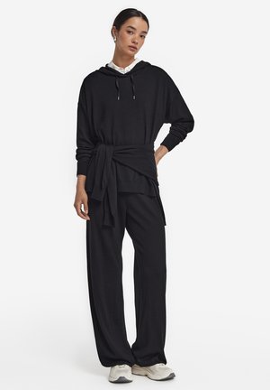 Ensemble lounge noir comprenant un hoodie décontracté avec une taille nouée et un pantalon large. Tissu doux avec un minimum de détails et une texture lisse.