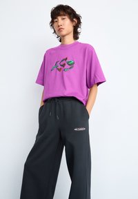T-shirt en coton violet avec un logo graphique sur la poitrine, associé à un pantalon de survêtement noir avec un petit logo et une taille élastique avec cordon.