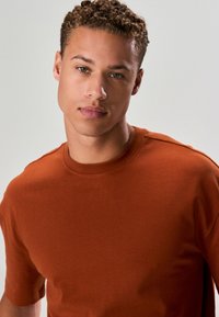 Kortärmad t-shirt i rostfärgad nyans tillverkad av mjukt tyg med rund halsringning och avslappnad passform, med minimala sömmar och rena linjer.