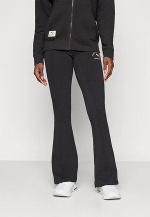 Black flared sweatpants in soft fabric with a fitted waist, featuring a subtle logo detail on the hip and contrasting stitching.