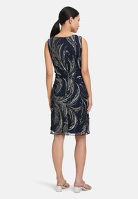 Robe sans manches bleu marine avec un motif paisley argenté fluide parsemé de sequins. Elle présente un ourlet au genou et une silhouette ajustée.