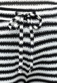 Κοντινό πλάνο υφάσματος πλεκτού με μαύρες και λευκές ρίγες, με δεμένο φιόγκο από κορδόνια τράβηγμα με ίδια ριγέ σχεδίαση.