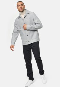 Veste en mélange de laine grise avec fermeture à boutons, deux poches avant et un col classique. Portée avec un pantalon noir et des baskets blanches.