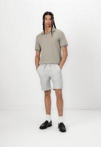 Kortermet polo i lys beige stoff med ribbet krage og mansjetter, kombinert med lysegrå shorts med elastisk midje og lommer.