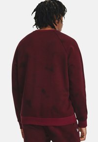 Sudadera de cuello redondo en color burdeos con textura acanalada, presenta mangas raglán y un dobladillo liso. Incluye un pequeño logotipo en la esquina inferior.