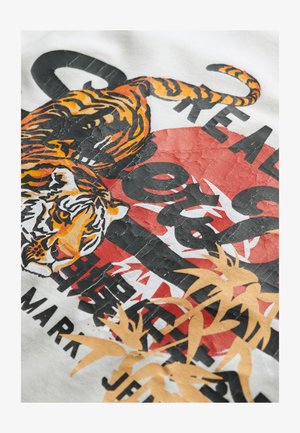Tessuto bianco con una grafica di una tigre in arancione e nero, circondata da accenti rossi e testo nero in grassetto, con un aspetto testurizzato.