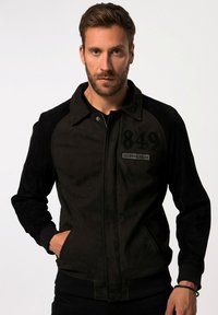 Sort bomberjakke med tekstureret stof, ribbede manchetter, to sidelommer og et patch med "849 FIGHTER PILOT" på brystet.