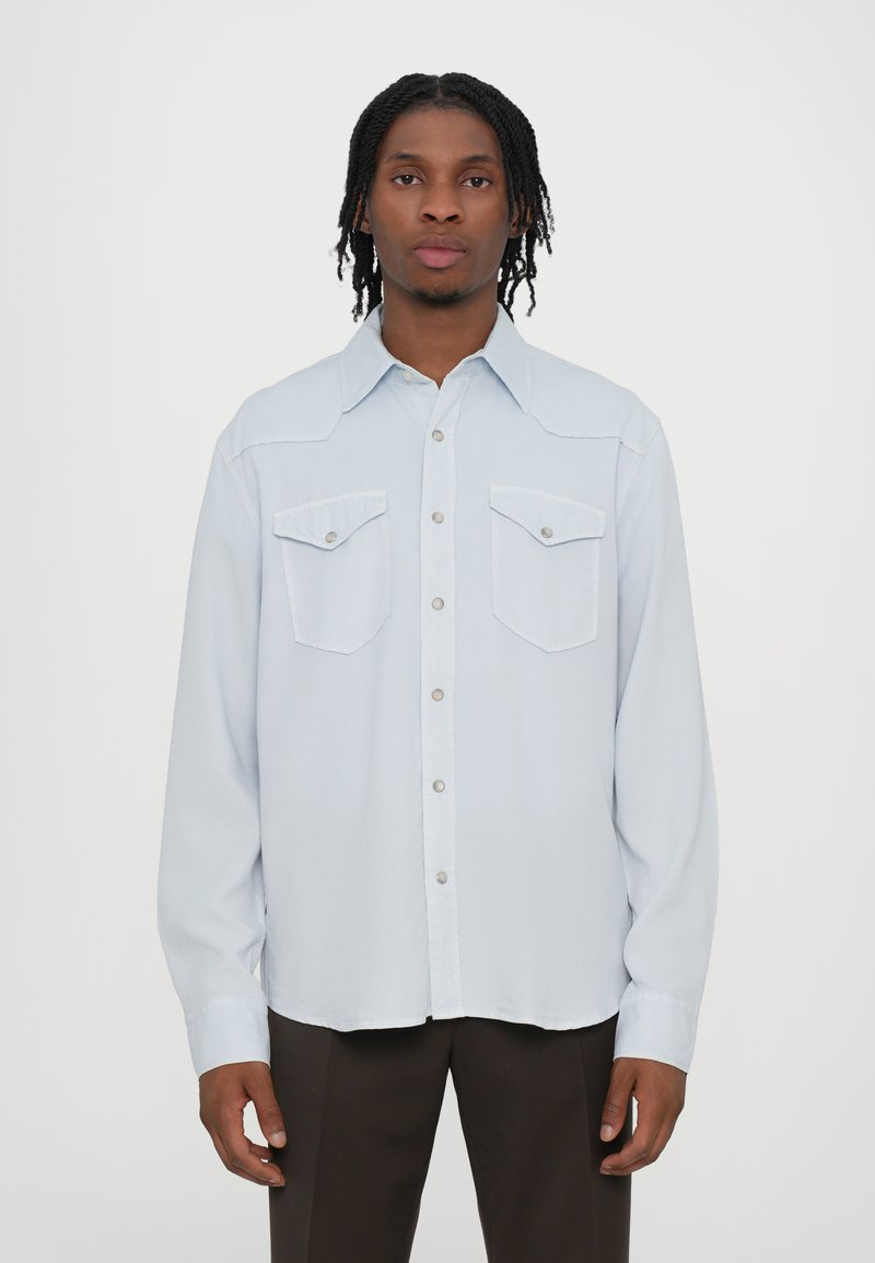 Svetlo modrá košela s dlhým rukávom, s gombíkmi na prednej strane, dvoma náprsníkmi a dizajnom v západnom štýle. Hladký textúra látky.