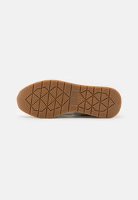 Brown rubber outsole with a textured, patterned surface and triangular traction elements. Smooth edges and a subtle logo imprint.