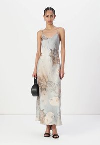 Abito maxi floreale grigio chiaro con motivi floreali più scuri. Spalline sottili, busto aderente e silhouette fluida. Borsa nera e tacchi.