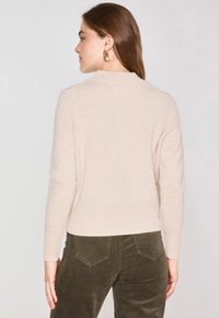 Pull en tricot beige clair avec un ourlet et des poignets côtelés, doté d'un col rond. Accompagné de pantalons en velours côtelé vert olive.