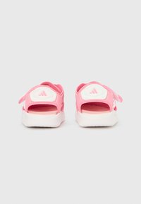 Ροζ αθλητικά σανδάλια με λευκές λεπτομέρειες, ρυθμιζόμενα λουριά με αυτοκόλλητο, ανοιχτή πλάτη και υφασμένα πέλματα· το λογότυπο εμφανίζεται στη φτέρνα.