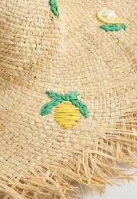 Sombrero de paja trenzada con bordes con flecos, que presenta bordados de piña y limón amarillos acentuados por hojas verdes. Color beige natural.