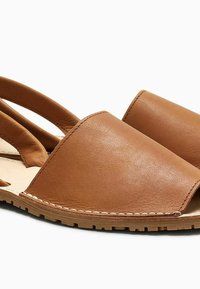 Sandali in pelle marrone con una larga fascia piatta per le dita e due fasce curve sul retro. Presentano una superficie texturizzata e dettagli cuciti.