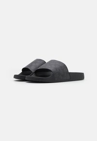 Chanclas negras con una parte superior texturizada y suela lisa, que presentan un diseño de punta abierta y un sutil detalle estampado en las correas.