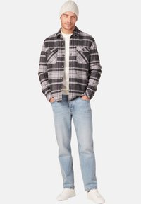 Gestrikte flanellen shirt in zwart, grijs en paars, met twee borstzakken. Gecombineerd met lichtblauwe jeans en witte sneakers. Gebreide beanie op het hoofd.