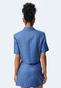 Blauwe blazer en rok set met korte mouwen in een gestructureerde stof. Kenmerkt zich door een getailleerde pasvorm, puntige kraag en zichtbare achternaden.