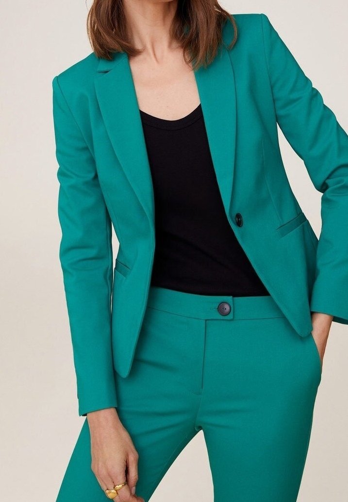 Turkusowy żakiet dopasowany, z pojedynczym guzikiem, w połączeniu z czarnym dopasowanym topem i spodniami. Gładka faktura z dobrze zorganizowanym krojem i ostro zakończonymi klapami.